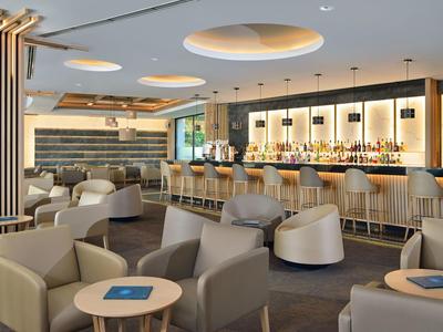 Modern hotel bar with comfortable armchairs, wooden tables, and elegant lighting.