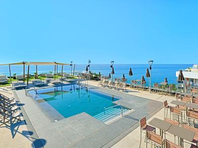 Modern pool area with sun loungers and sea view under clear sky.