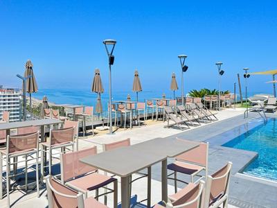 Taras na dachu z basenem, stołami, krzesłami i widokiem na morze przy czystym niebie.