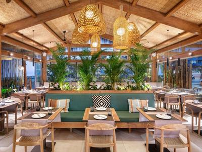 Licht, modern restaurant met houten accenten, planten en hanglampen.