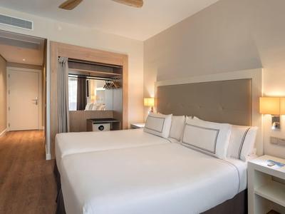 Modern hotel room with two single beds, bedside lamps, and wooden flooring.