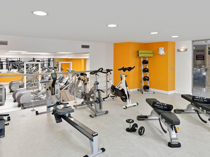 Brightly lit gym with modern equipment and dumbbells in a hotel.