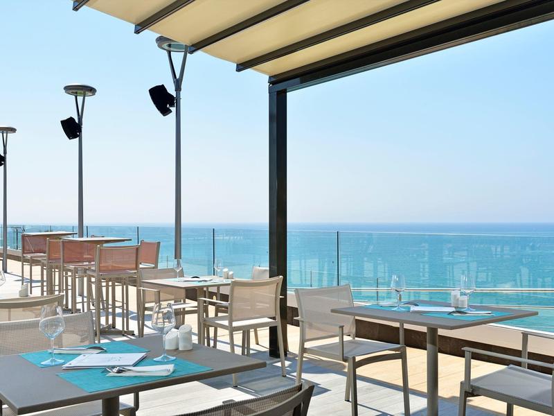 Terrace with tables and chairs overlooking the sea under a clear sky.