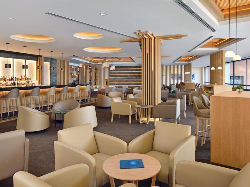 A bright, modern hotel bar area with comfortable armchairs and a long counter.