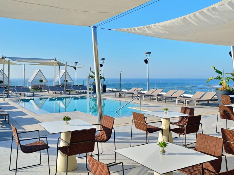 Modern terrace with tables, chairs, pool, and sea view on a clear day.