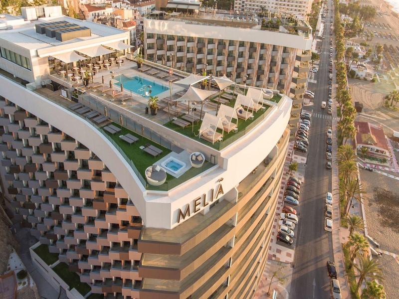 Luxury hotel with rooftop pool next to a main road and a sandy beach nearby.