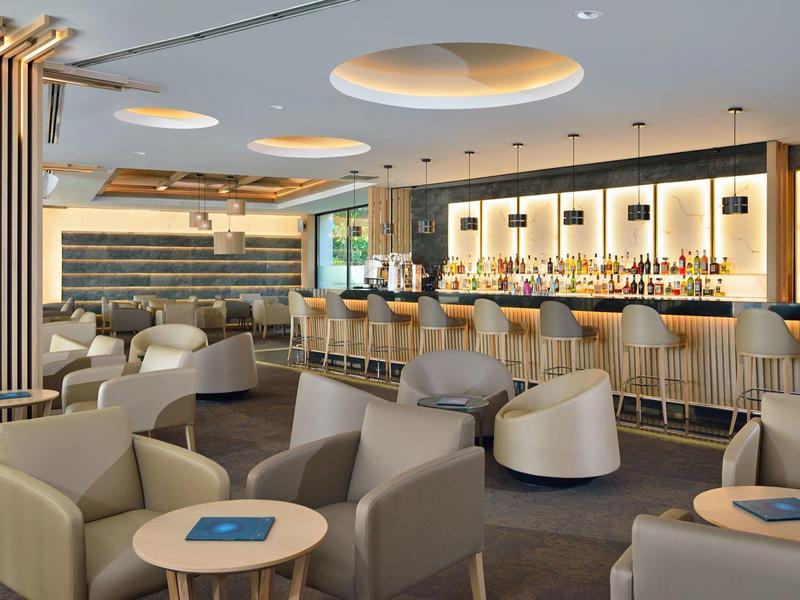 Modern hotel bar with comfortable armchairs, wooden tables, and elegant lighting.