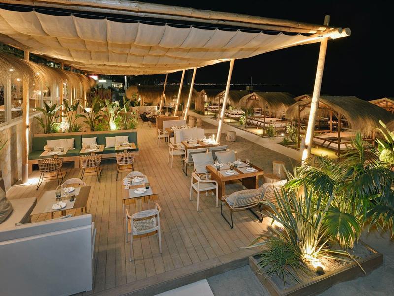 Cozy outdoor restaurant terrace with wooden floor, tables, and plants at night.