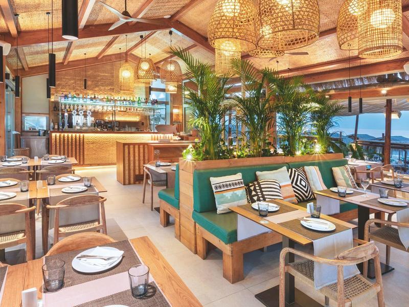 Modern restaurant with wooden furniture, green benches, and sea view.