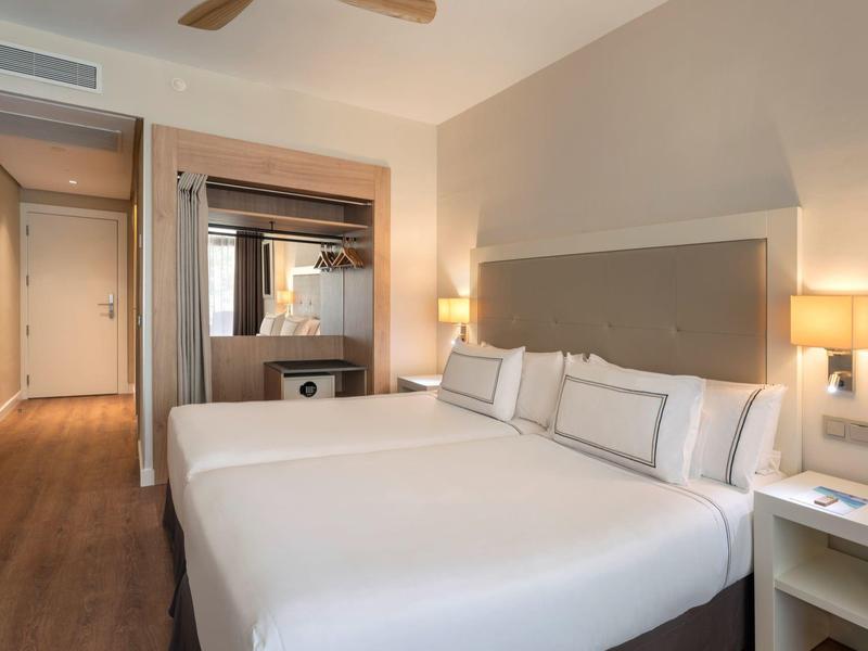 Modern hotel room with two single beds, bedside lamps, and wooden flooring.