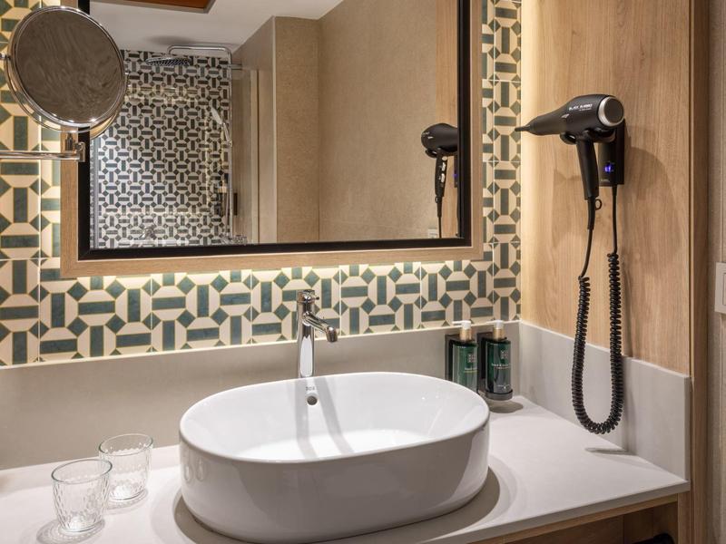 Modern bathroom with round sink, large mirror, and wall-mounted hairdryer.