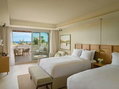 Modernes Hotelzimmer mit zwei Betten, hellen Holzmöbeln und Terrasse mit Meerblick.