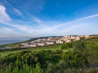 Dorf mit weißen Häusern auf grünem Hügel unter blauem Himmel mit Wolken.