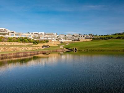 Seeblick auf Golfplatz mit grünem Rasen, Brücke und moderner weißer Gebäude am Hang.