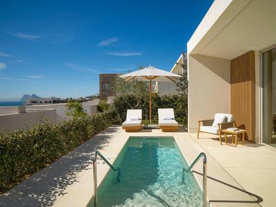 Moderner Außenbereich mit kleinem Pool, Liegestühlen, Sonnenschirm und Meerblick im Hintergrund.