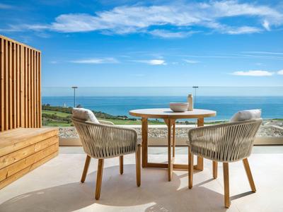 Terrace with two chairs and a table overlooking the sea under a blue sky.