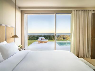 Helles Schlafzimmer mit großem Bett, Schiebetür und Blick auf Terrasse mit Pool und Meer im Hintergrund.