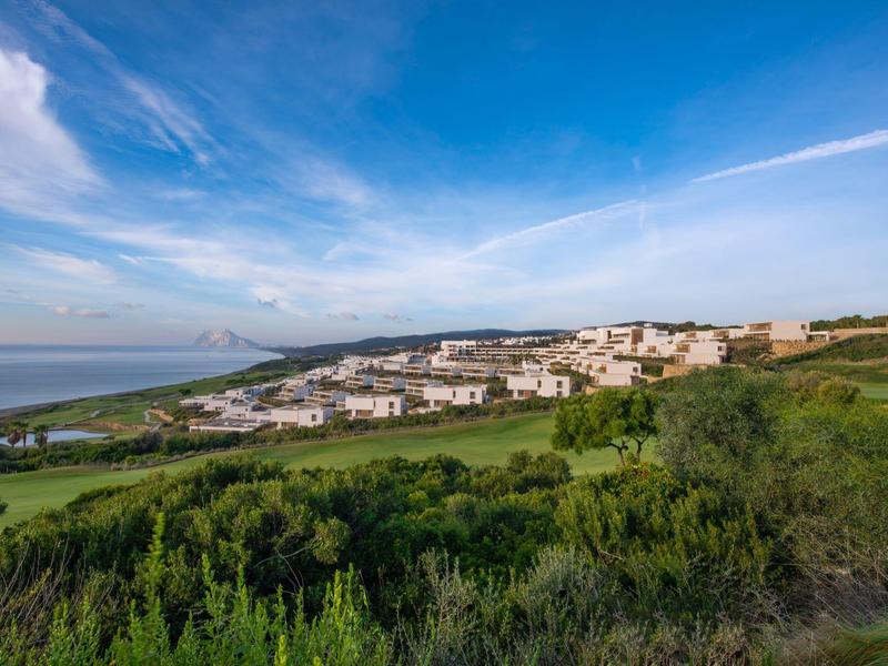 Dorf mit weißen Häusern auf grünem Hügel unter blauem Himmel mit Wolken.