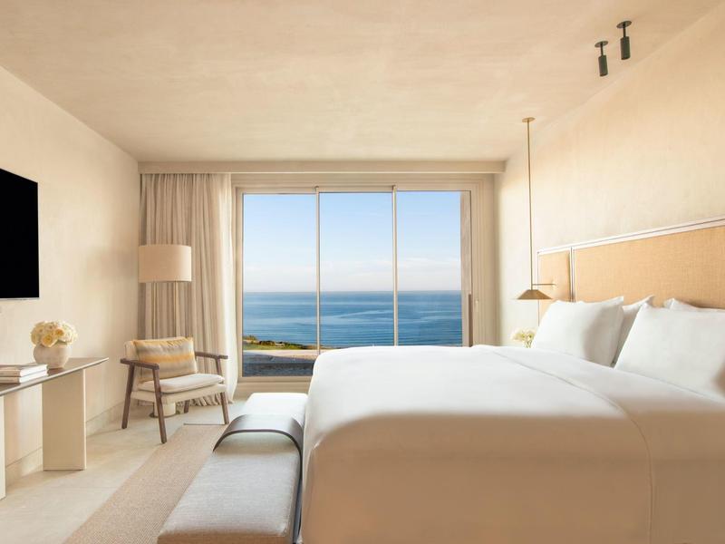 Helles Schlafzimmer mit großem Bett, Meerblick durch bodentiefe Fenster und minimalistischer Einrichtung.