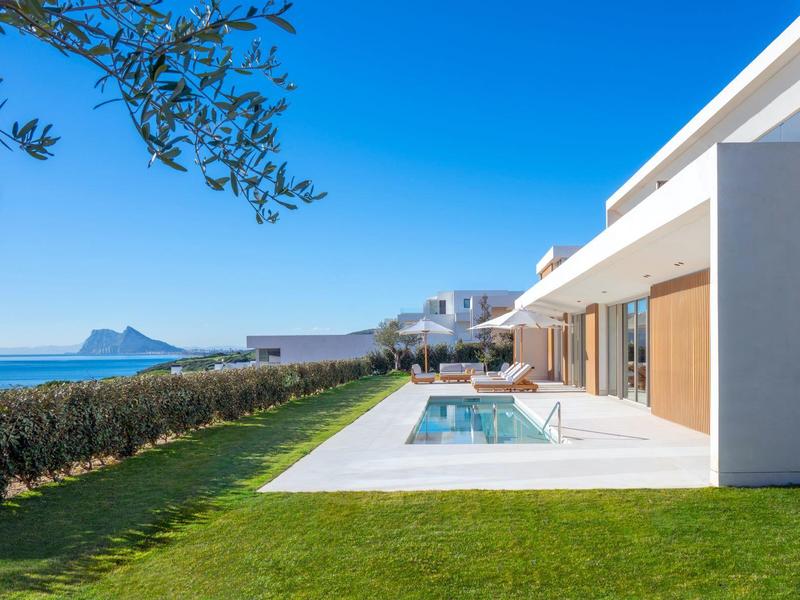 Moderner weißer Wohnhaus-Komplex mit Pool, grünem Rasen und Meerblick unter blauem Himmel.