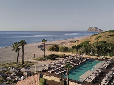 Piscina dell'hotel con sdraio, palme e vista su una lunga spiaggia sabbiosa e il mare.