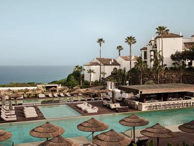 Piscina moderna dell'hotel con ombrelloni e vista sul mare in una giornata di sole.