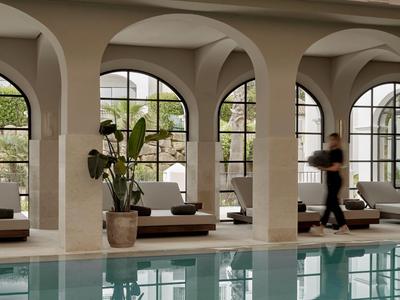 Piscina con archi in pietra, lettini e grande finestra con luce naturale.