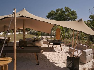 Area salotto esterna con mobili moderni sotto una grande tenda beige.