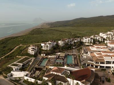 Vista aerea di un hotel costiero con piscina e colline verdi sullo sfondo.