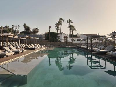 Piscina dell'hotel al tramonto con lettini e palme, tranquilla e invitante.