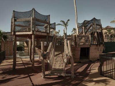 Parco giochi in legno con ponte sospeso e torri di osservazione sotto il cielo blu