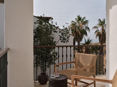 Balkon z dwoma drewnianymi krzesłami, małym stolikiem i widokiem na palmy pod czystym niebem.