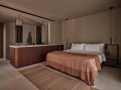 Nowoczesny pokój hotelowy z podwójnym łóżkiem, brązową narzutą i pośrednim oświetleniem.