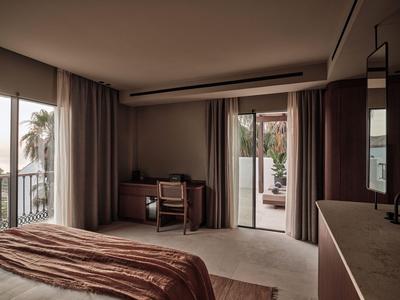 Nowoczesny pokój hotelowy z biurkiem, fotelem i balkonem z widokiem na palmy.