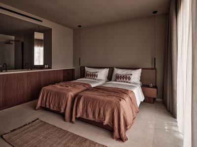 Camera d'hotel moderna con due letti singoli, coperte marroni e tende sulla parete destra.