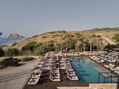 Piscina dell'hotel con lettini, circondata da colline e vista mare sotto un cielo limpido.