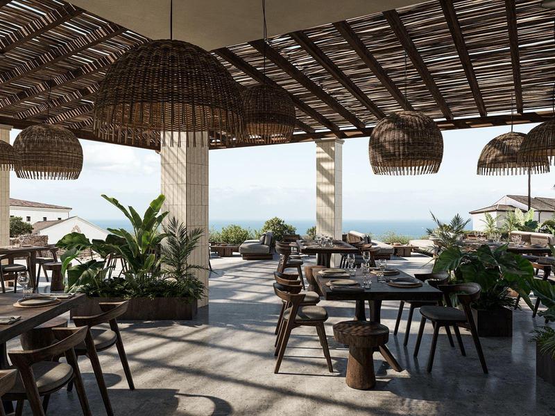 Área de restaurante al aire libre con sillas de madera, mesas y vista al mar bajo un techo de paja.