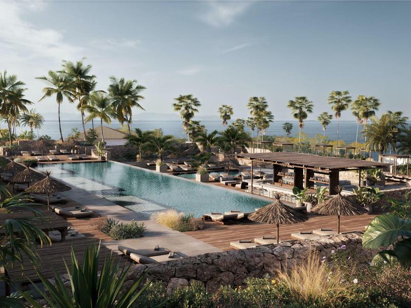 Piscina grande al aire libre rodeada de palmeras y áreas de descanso junto al mar.