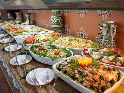 Buffet mit vielfältigen Salaten und Gemüse in großen weißen Schüsseln auf einer langen Theke.