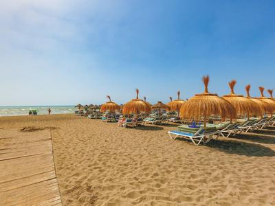Strand mit Sonnenschirmen und Liegen, blauer Himmel, heller Sand und ruhiges Meer im Hintergrund.