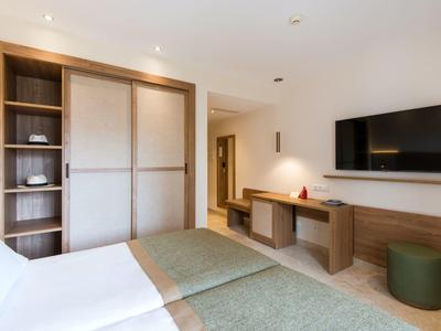 Modernes Schlafzimmer mit Doppelbett, Holzmöbeln, großem Schrank und Wandfernseher in hellen Farben.