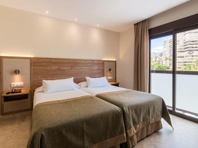 Modernes Schlafzimmer mit zwei Einzelbetten, Holz-Kopfteil und großer Glas-Schiebetür zum Balkon.