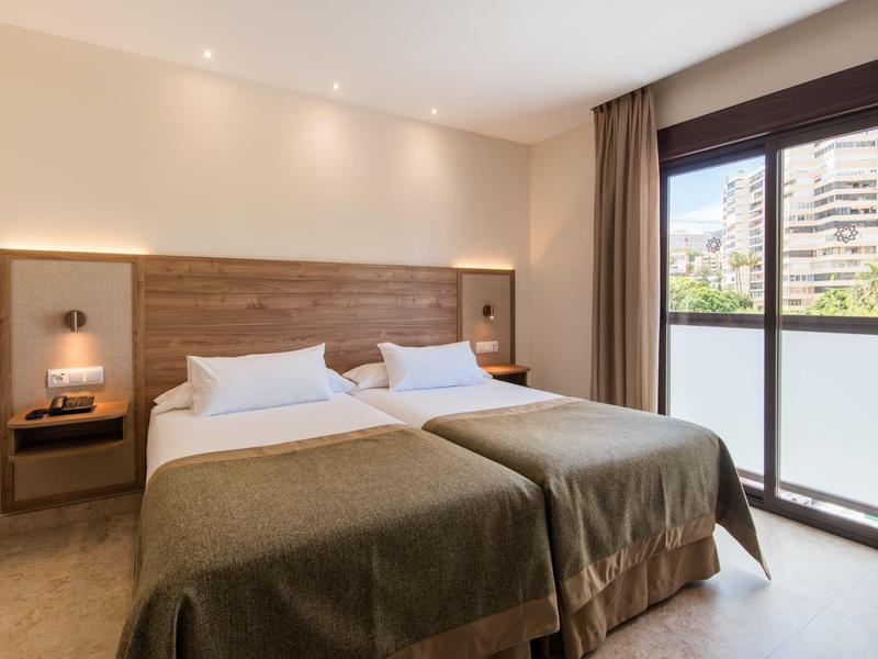 Bright hotel room with two single beds and a large window overlooking the city.