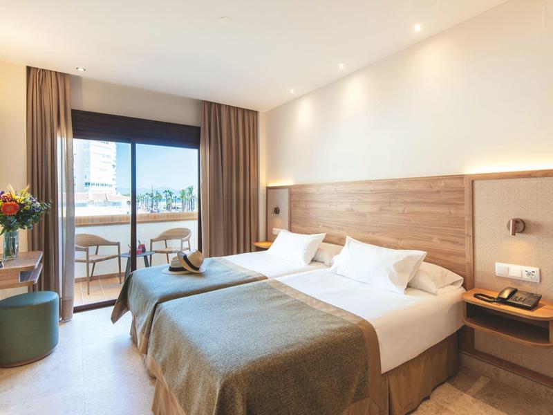 Modern hotel room with double bed, balcony, and elegant interior in daylight.