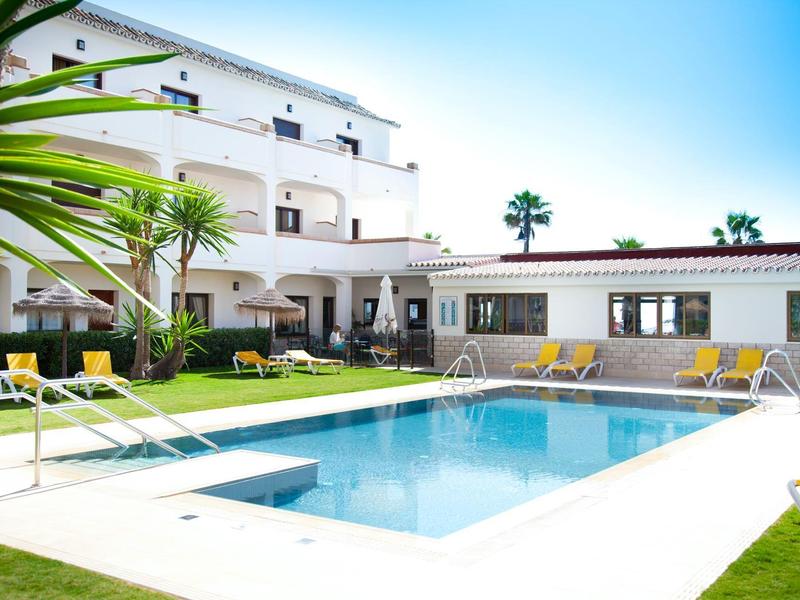 Modern hotel pool with sun loungers and palm trees under a clear sky.