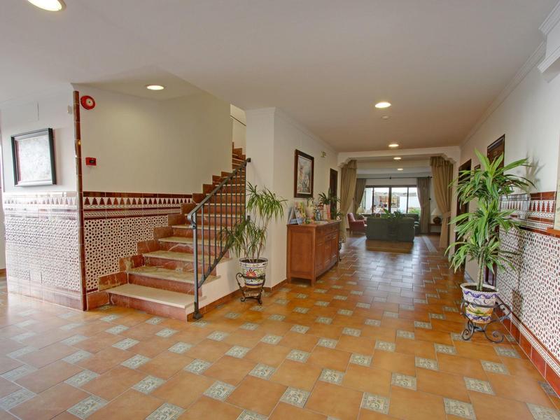 Spacious, bright hotel hallway with tiled floor, staircase, and decorative plants.