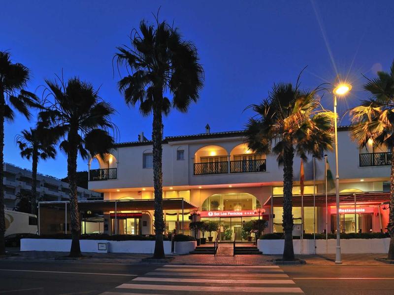 Ein beleuchtetes Gebäude mit Palmen davor, aufgenommen in der Dämmerung.