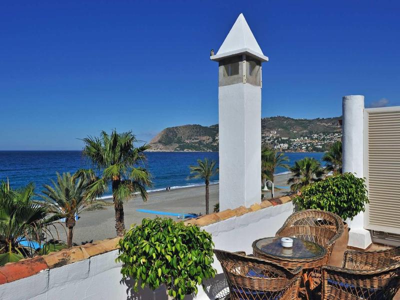 Terrasse mit Korbstühlen, grünen Pflanzen und Meerblick unter klarem blauem Himmel.
