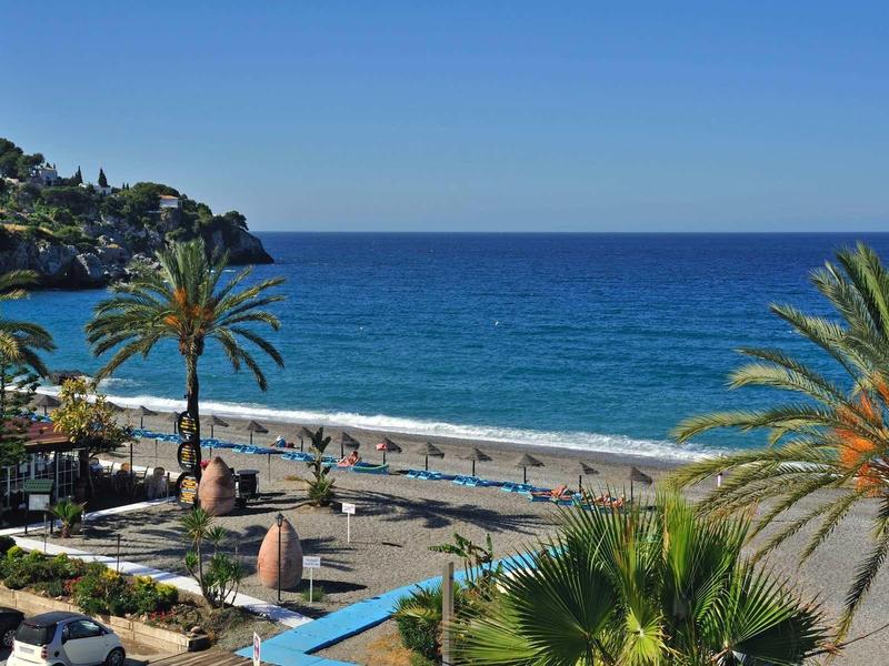 Blick auf einen Strand mit Palmen, blauem Meer und klarem Himmel bei Sonnenschein.