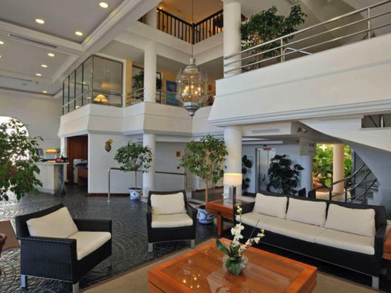 Großer heller Raum mit moderner Sitzgruppe aus dunklem Holz und cremefarbenen Kissen, Pflanzen und Treppe.